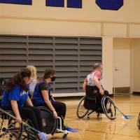 Adults in wheelchairs playing floor hockey.